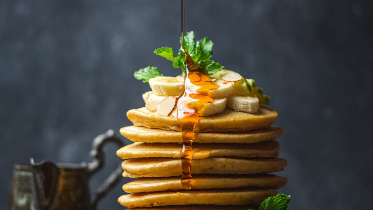 Stack of golden banana oat pancakes topped with sliced bananas and a drizzle of maple syrup