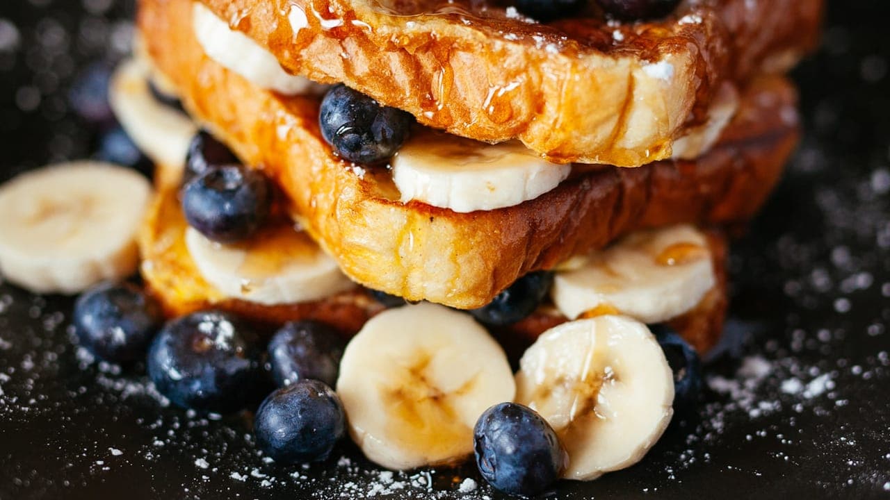 Stack of golden French toast slices dusted with powdered sugar and topped with fresh berries and maple syrup