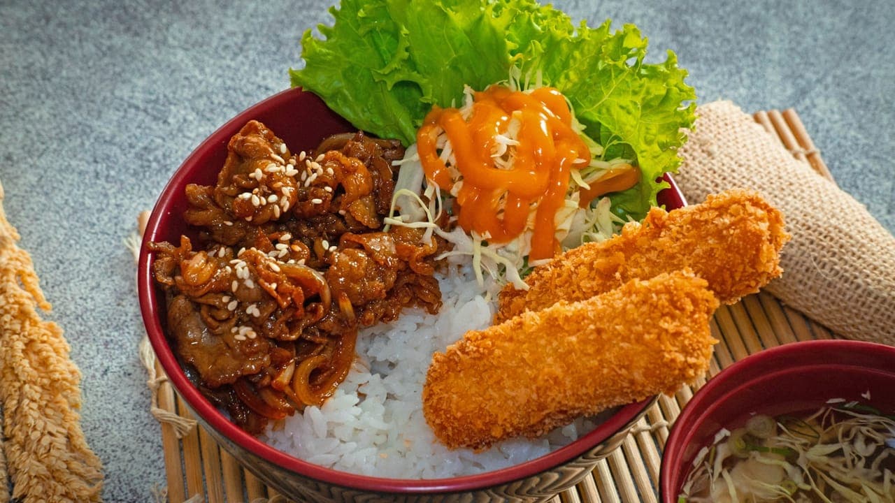 Meal prep containers with sliced teriyaki chicken, rice, broccoli, and shredded carrots